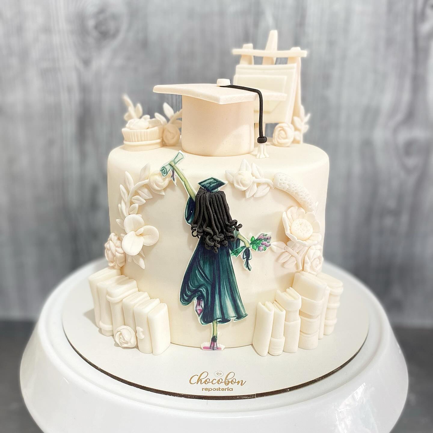 Torta de grado con silueta de graduada modelada a mano, libros y flores en azúcar