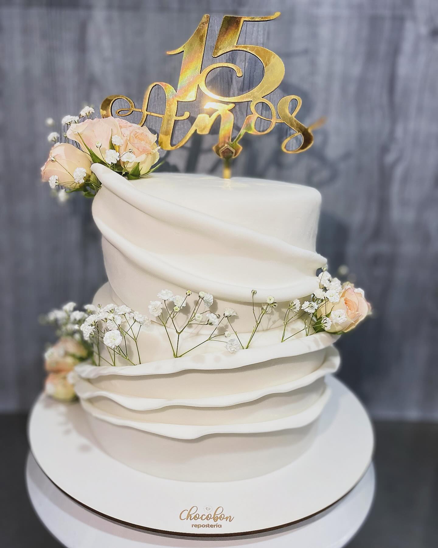 Torta de 15 años en blanco con drapeado de fondant, rosas durazno y gypsophila